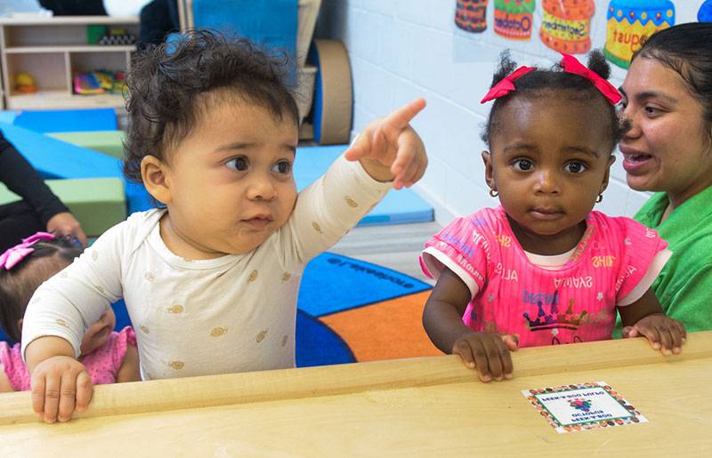Two young children at a wooden table in a colorful playroom